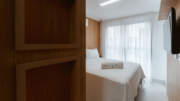 A hotel room with a bed, a television, and a window with curtains. - Master Luxo Jardins Almare - By Almare (João Pessoa)