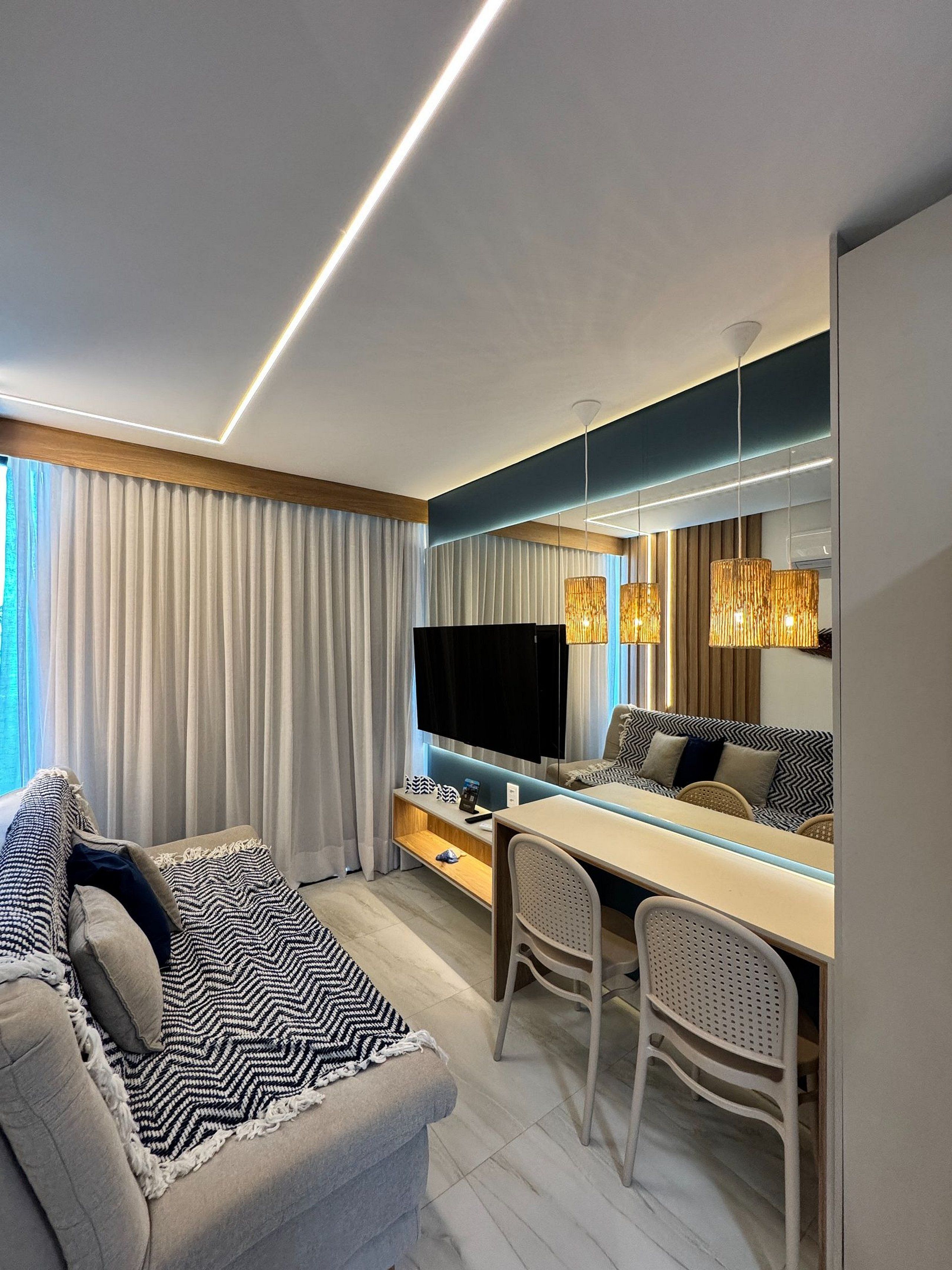 Ein modernes Hotelzimmer mit einer Sitzecke, Esstisch, Stühlen, einem Fernseher und einem großen Fenster mit Vorhängen.