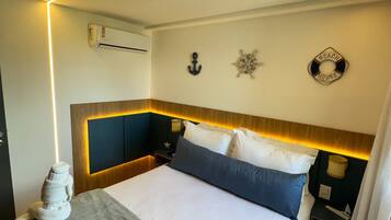 Habitación de hotel con cama, cabecero, aire acondicionado de pared, decoración en la pared y mesita de noche con lámpara.