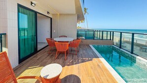 Ein Poolbereich mit Tisch und Stühlen, Blick auf das Meer und ein Gebäude im modernen Stil.