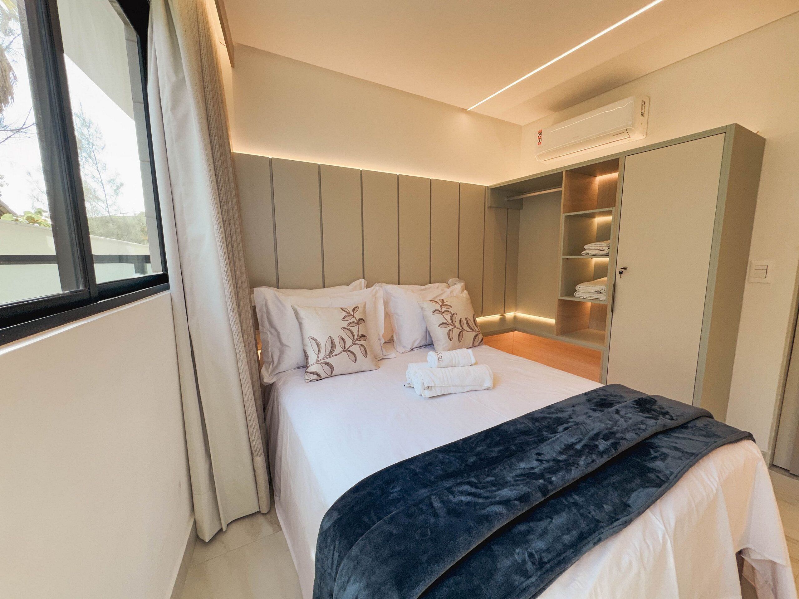 A modern bedroom with a bed, a wardrobe, and an air conditioning unit.
