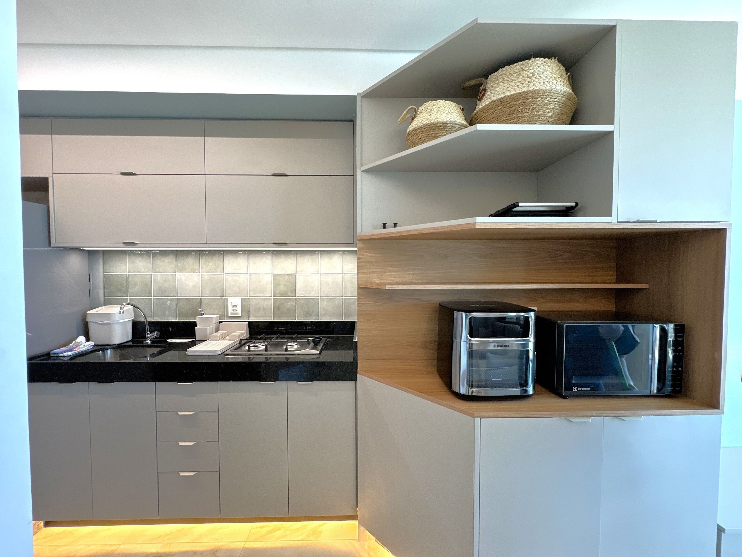 Una cocina moderna con gabinetes grises, encimera negra, microondas empotrado y un lavamanos pequeño.