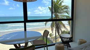 Ein Zimmer mit großem Fenster und Meerblick, einem runden Tisch und zwei Stühlen.