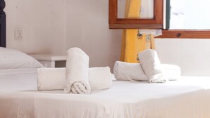 Een net opgemaakt bed met opgerolde witte handdoeken, een houten hoofdbord en een raam met uitzicht.