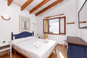 Un dormitorio con cama, mesitas de noche, un escritorio, un espejo y una ventana con cortinas.
