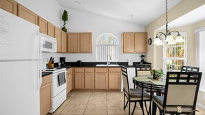 A modern kitchen with wooden cabinets, a dining area with a glass table, and a large window with a view. - Indian Creek Beautiful 4 Bedroom 3 Bathroom Villa Close to Disney (Kissimmee)