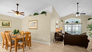 A spacious living area with a dining table, chairs, a sofa, ceiling fans, and a large window. - Indian Creek Beautiful 4 Bedroom 3 Bathroom Villa Close to Disney (Kissimmee)