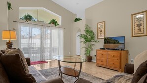 A living room with a sofa, a glass coffee table, a TV on a wooden cabinet, and a potted plant. - Indian Creek Beautiful 4 Bedroom 3 Bathroom Villa Close to Disney (Kissimmee)