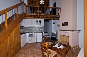 Eine Küche mit weißen Schränken, einem Esstisch mit Stühlen, einem Kamin und einer Holztreppe.