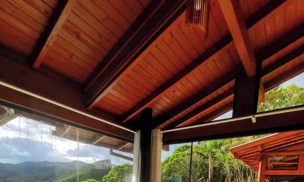 A wooden ceiling with a view of lush greenery and mountains through large windows.