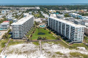 Een hoog hotel met meerdere balkons, een centrale binnenplaats met een zwembad, en een strandgedeelte op de voorgrond.