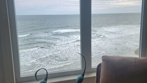 Ein Zimmer mit großem Fenster und Meerblick, ein braunes Sofa und zwei Stehlampen.