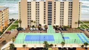 Ein mehrstöckiges Hotel mit Tennisplatz und Meerblick.
