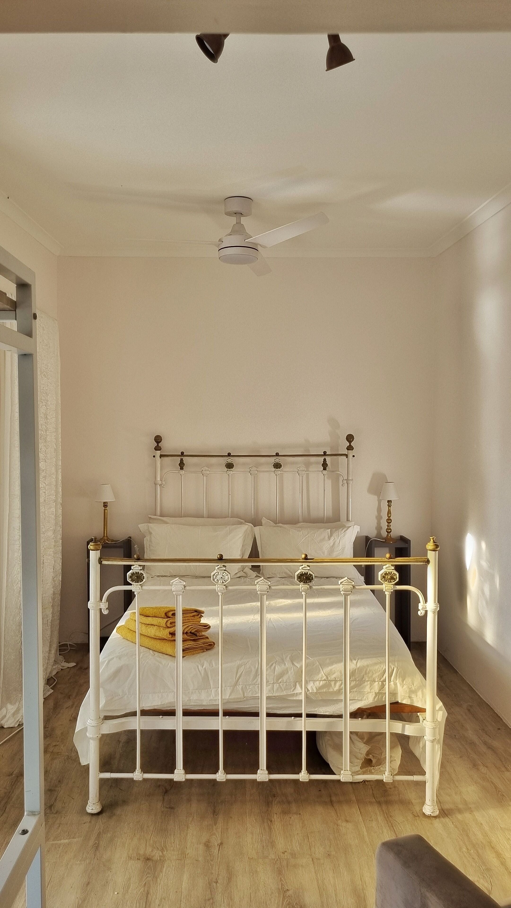 A white metal bed with a headboard, a ceiling fan, and a wooden floor.