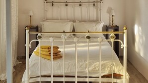 Een wit metalen bed met hoofdeinde, een plafondventilator en een houten vloer.