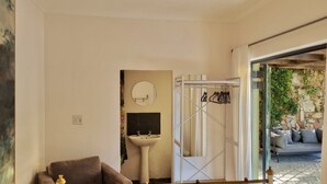 Een badkamer met een wastafel, spiegel en douche. Er is een bank en uitzicht op een buitenruimte met planten.