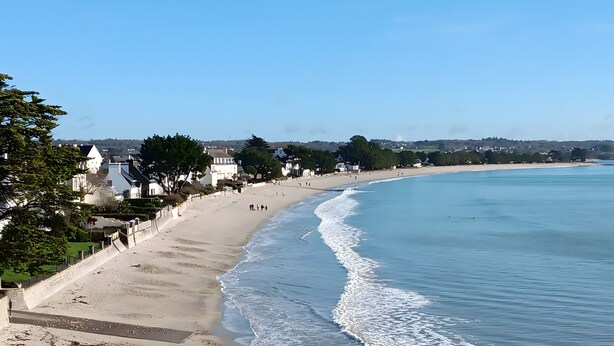Una playa con vistas claras al océano, una orilla de arena y una hilera de casas a lo largo de la playa.