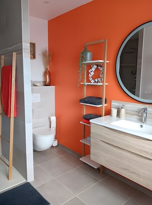 Un baño con inodoro blanco, lavamanos con espejo y repisas con adornos.