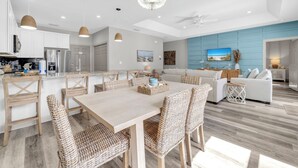 A modern kitchen with white cabinets, stainless steel appliances, and a dining area with wicker chairs and a wooden table. - 🏖️Walk to Beach | Great Location | Fire Pit | Sandy Shores🏖️ (Panama City Beach)