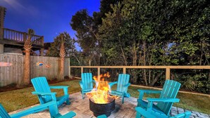 A backyard with a fire pit, four blue Adirondack chairs, and a wooden deck. - 🏖️Walk to Beach | Great Location | Fire Pit | Sandy Shores🏖️ (Panama City Beach)