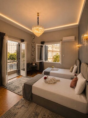 Une chambre d’hôtel avec deux lits, un lustre, un balcon avec vue et un bureau agrémenté d’un vase.