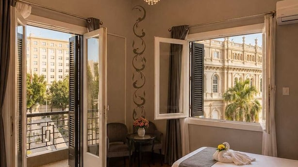 A hotel room with two beds, a chandelier, a balcony with a view of buildings, and a small table with chairs. - Garden City Tahrir Downtown (Cairo)