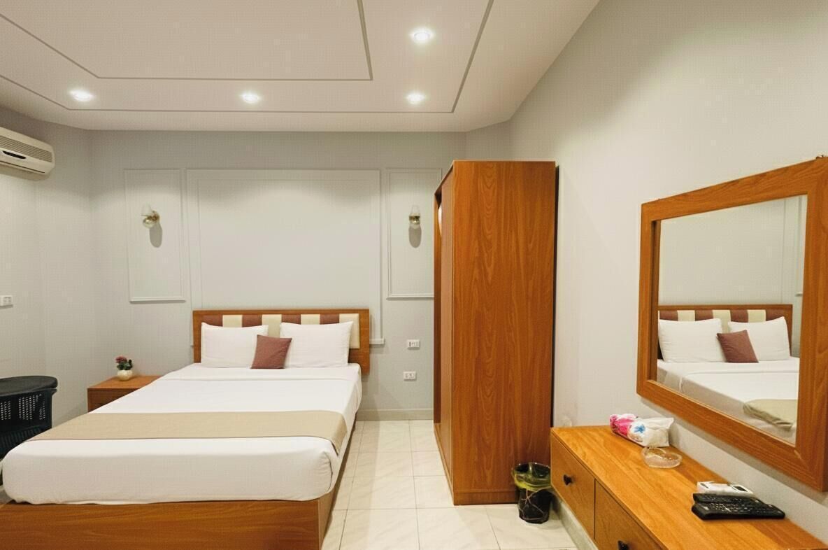 Een hotelkamer met een tweepersoonsbed, een houten garderobe, een nachtkastje met een afstandsbediening en een spiegel aan de muur.