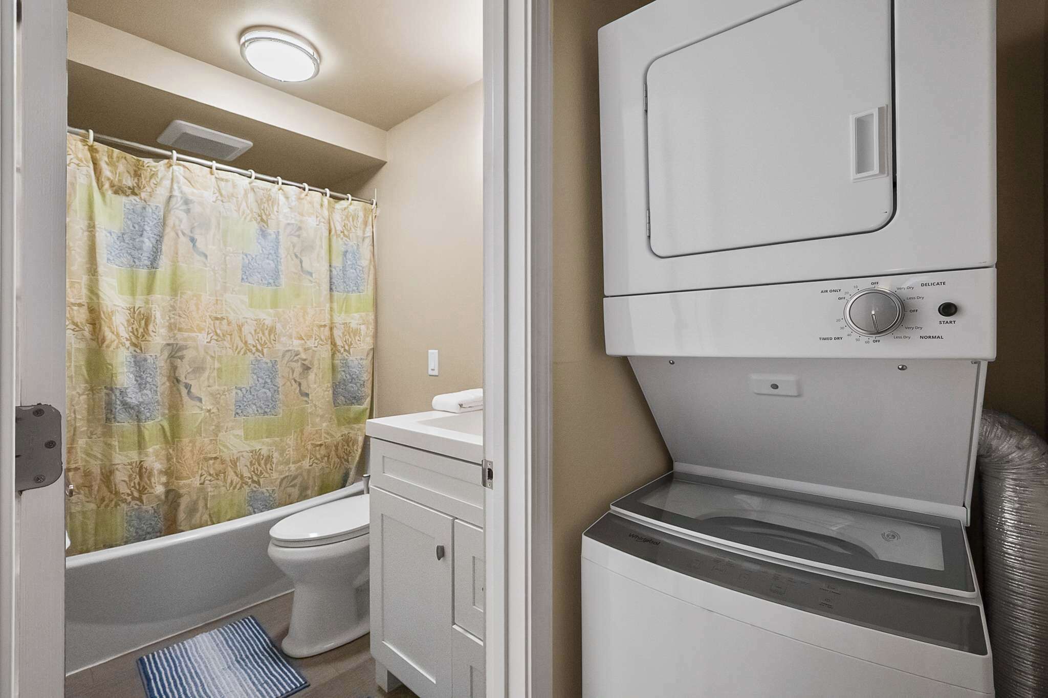 A compact bathroom with a shower curtain, toilet, and a stacked washer and dryer unit.