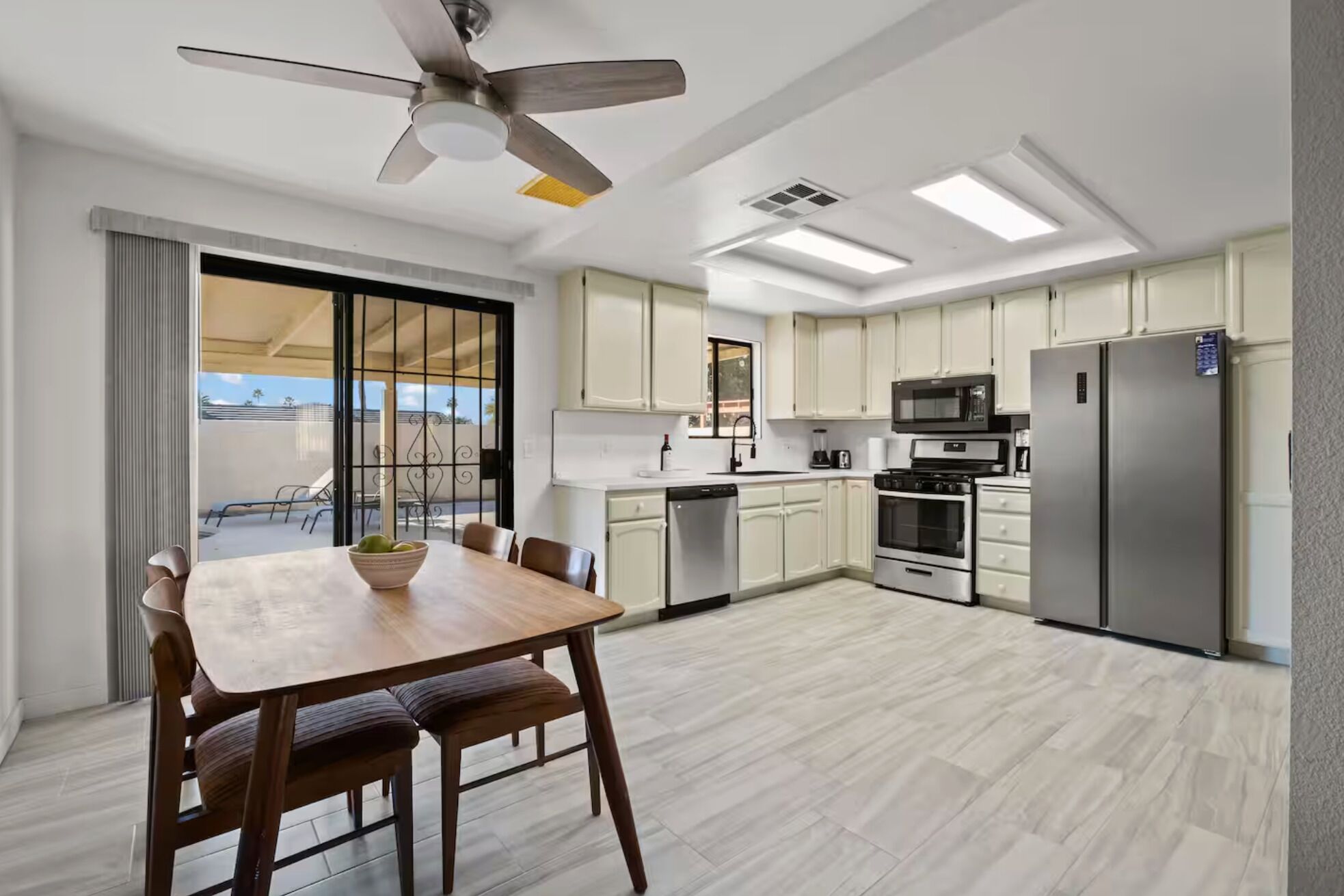 A modern kitchen with a dining area, including a table with chairs, a ceiling fan, and a view through a sliding door.