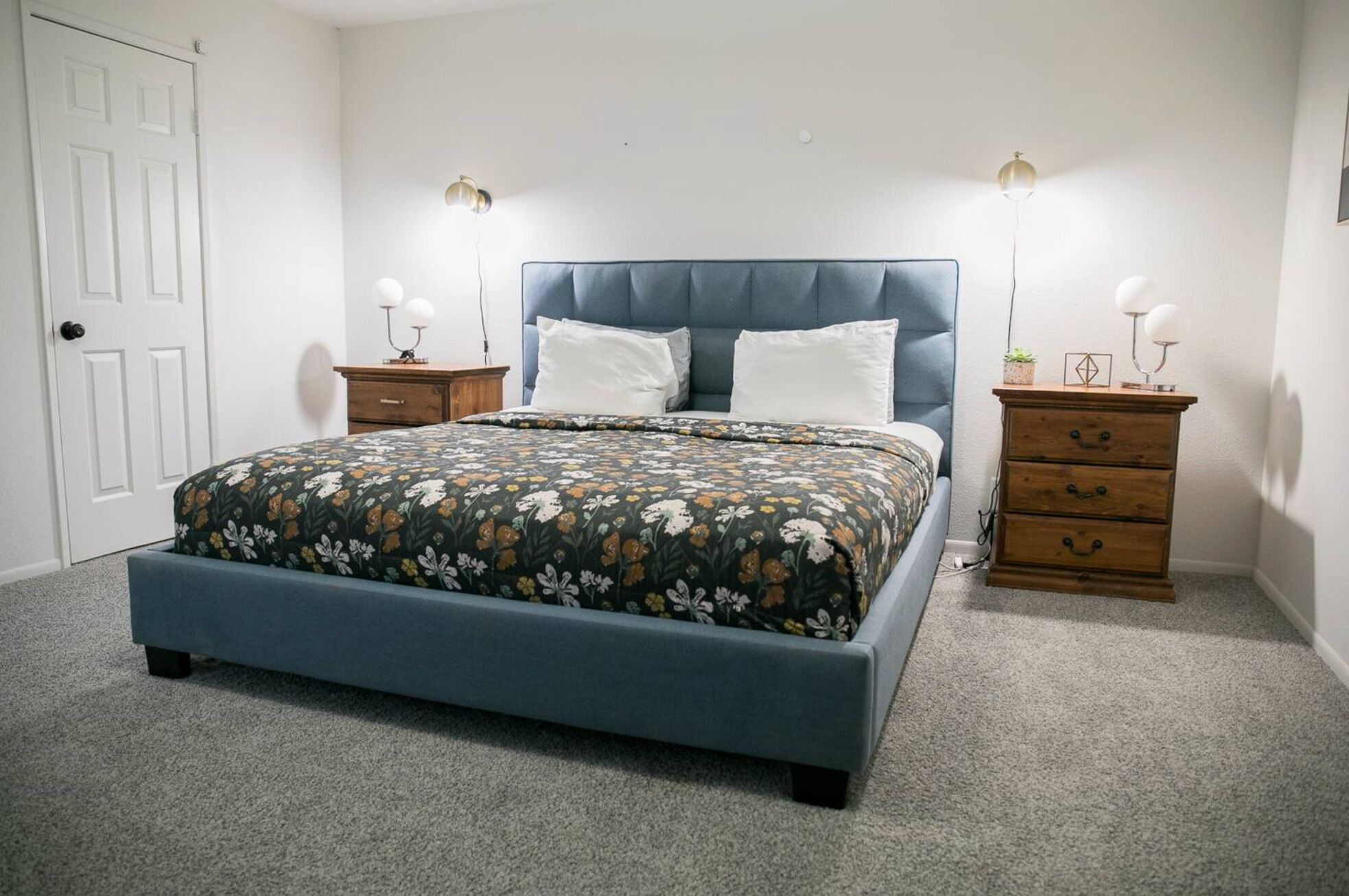 Un dormitorio con una cama, dos mesitas de noche, un aparador y una puerta.