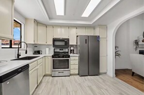 A modern kitchen with white cabinets, stainless steel appliances, and a skylight. - Monthly Palm Springs Oasis: Pool & Workspace (Cathedral City)