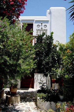 A white building with a door and windows, surrounded by potted plants and a stone pathway. - Villa Pinelopi (Mykonos)