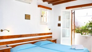 A bedroom with a wooden bed, a bedside table, a window, and a door leading to an outdoor area. - Villa Pinelopi (Mykonos)