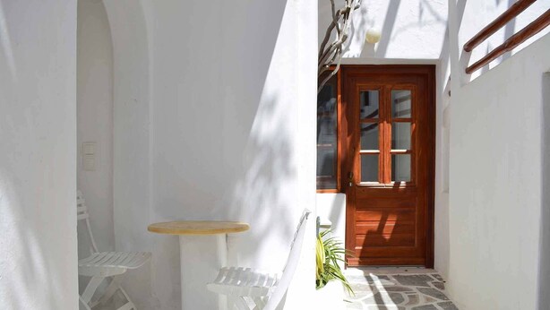 A narrow corridor with a wooden door, a small round table, and a white chair. - Villa Pinelopi (Mykonos)