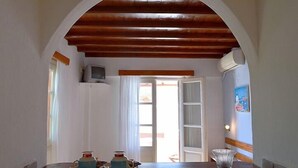 A room with a wooden ceiling, a television, a table with a vase, and a door leading outside. - Villa Pinelopi (Mykonos)