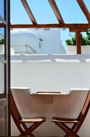 A balcony with a white wall, wooden beams, and two wooden chairs. - Villa Pinelopi (Mykonos)