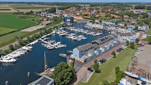 Un puerto deportivo con barcos amarrados, un edificio de fachada azul y un campo verde al fondo.