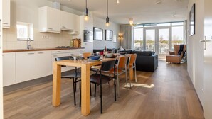 Una cocina moderna con armarios blancos, una mesa de comedor con sillas y una sala de estar con sofá y sillones.