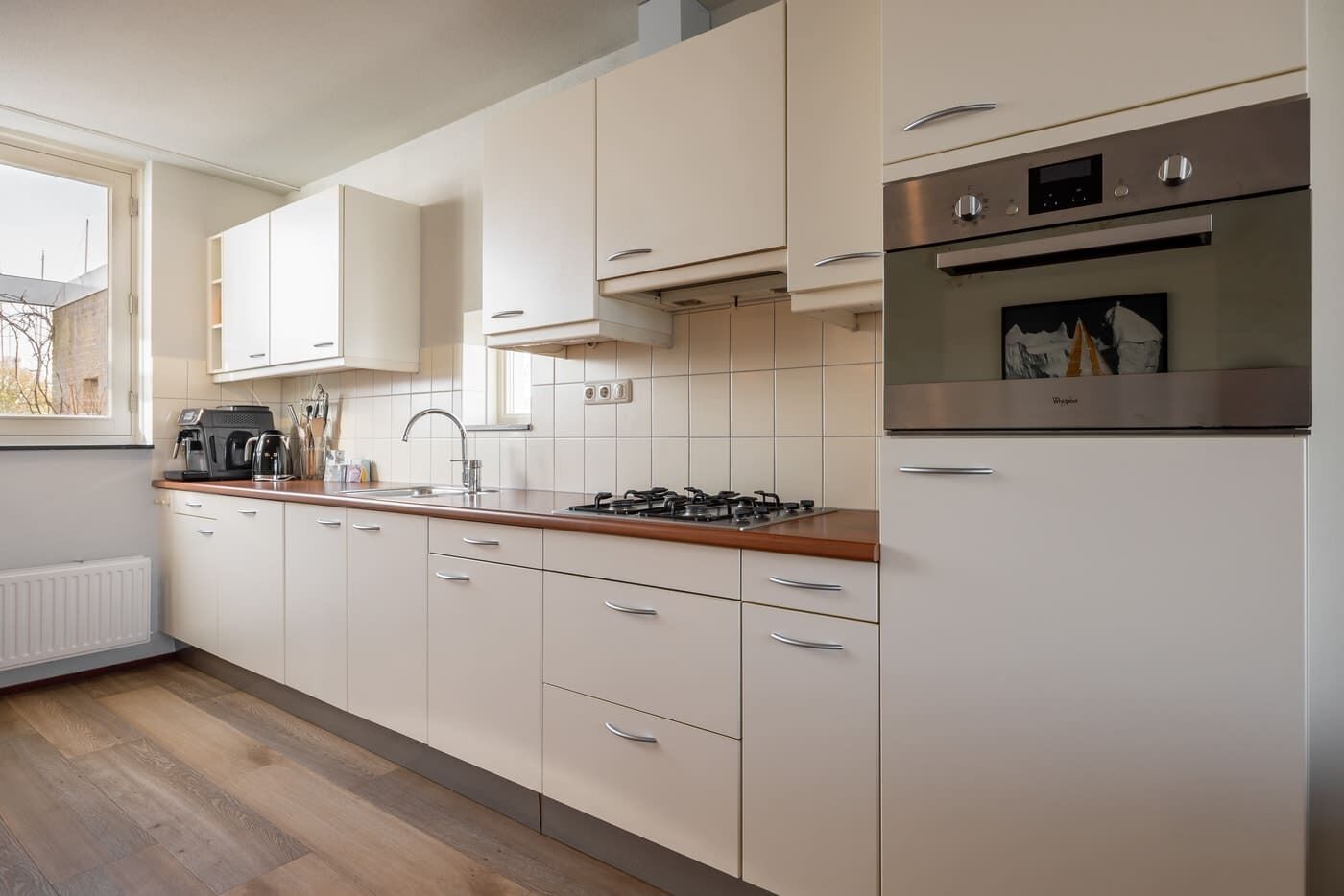 A modern kitchen with white cabinets, a gas stove, a built-in oven, and a window with a view.