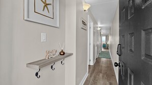 Um corredor com uma prateleira de madeira, uma decoração de estrela-do-mar, uma placa com a palavra 'Hello', um vaso e uma porta com superfície texturizada.