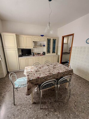 A compact kitchen with a dining table, chairs, and a hanging light fixture.