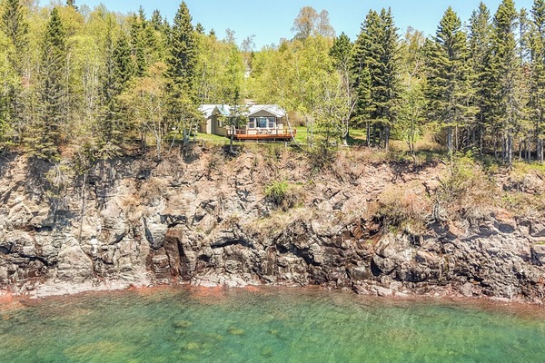 Waterfront property nestled atop rugged cliffs overlooking crystal-clear lake waters, surrounded by towering evergreens and seasonal foliage, offering a secluded and scenic lakeside retreat.