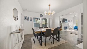 Un comedor moderno con una mesa de madera, sillas negras, una araña y una chimenea.