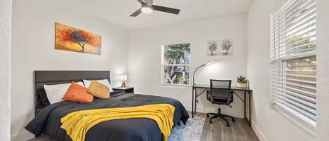 A bedroom with a bed, a desk, a ceiling fan, and a window with blinds.