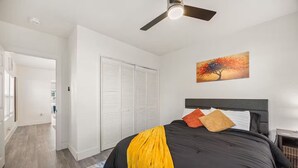 Un dormitorio con cama, ventilador de techo, un cuadro y armario.