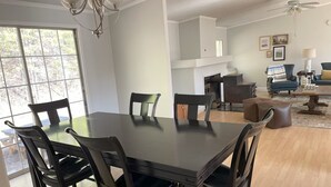 A dining area with a dark wooden table and chairs, a ceiling fan, and a view of the outdoors through large windows. - Spacious, Sunlit, 3 Bedroom, 2 Bath Home in East Asheville (Asheville)