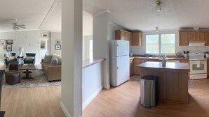 A modern kitchen with wooden cabinets, a central island, and a dining area with a sofa and chairs. - Spacious, Sunlit, 3 Bedroom, 2 Bath Home in East Asheville (Asheville)