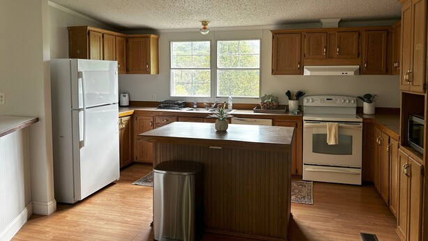 A kitchen with wooden cabinets, a stainless steel trash can, a refrigerator, a stove, and a window. - Spacious, Sunlit, 3 Bedroom, 2 Bath Home in East Asheville (Asheville)