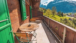 Un balcón de madera con una mesa y sillas, con vista a un paisaje montañoso.