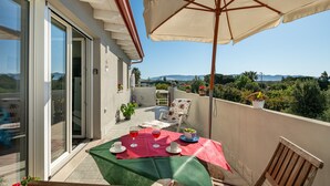 Un balcon avec une table dressée pour deux personnes, une chaise et un grand parasol.